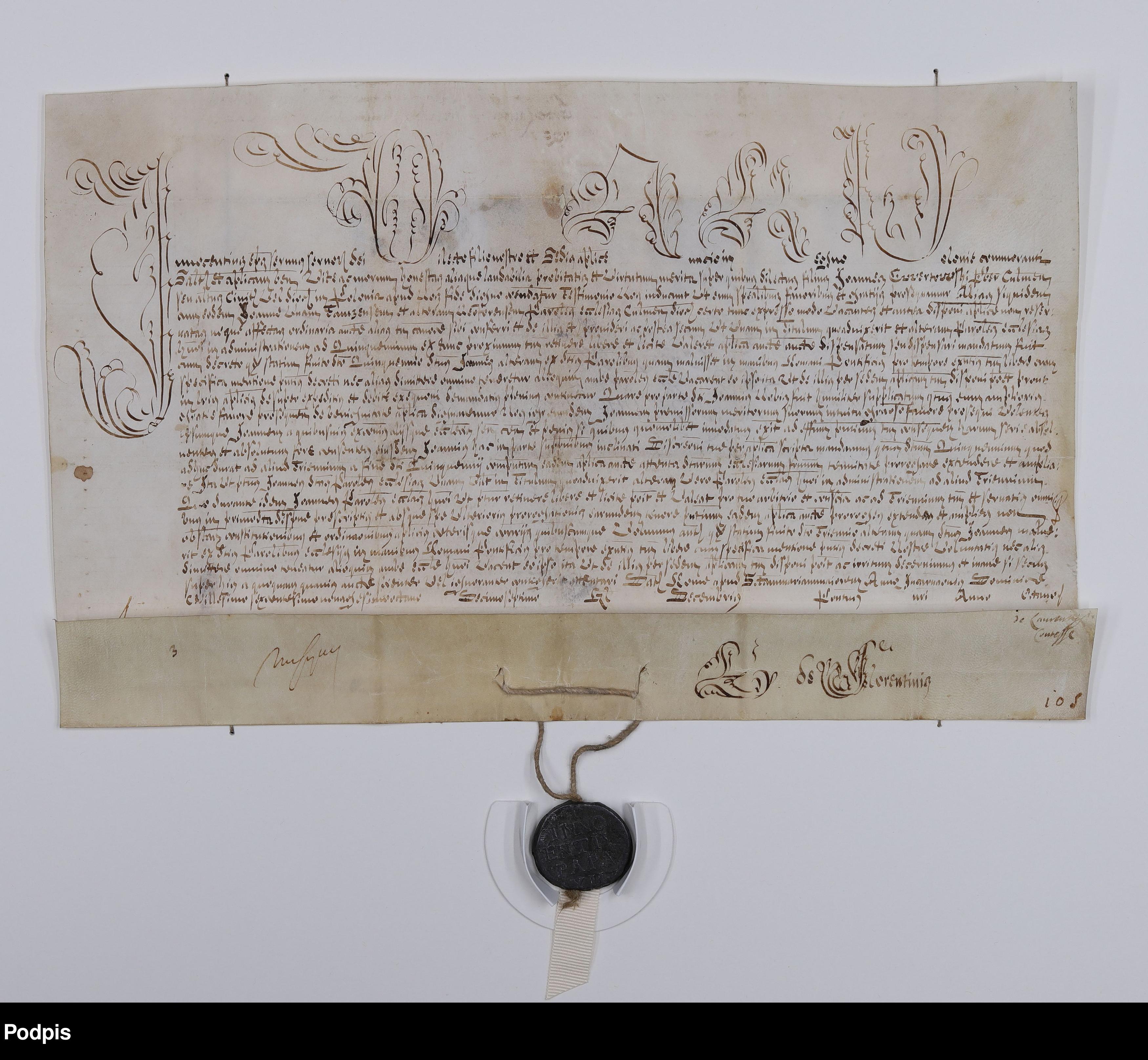 Dokument archiwalny zapisany odręczniem z ozdobnymi inicjałami na górze tekstu. Dół karty złożony, tam też widoczna zamocowana a sznurze pieczęć woskowa.