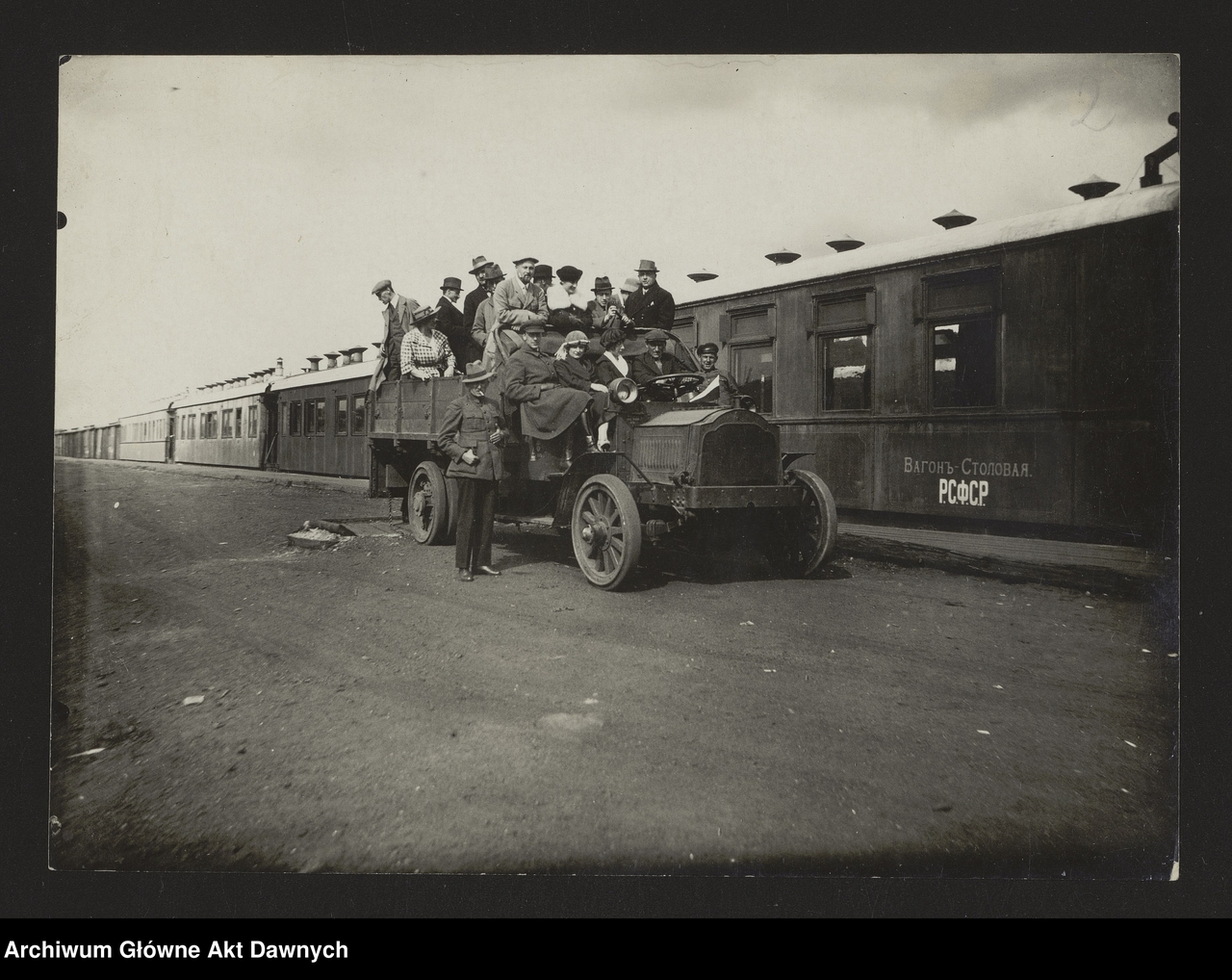 Fotografia przedstawia delegację polską siedzącą na ciężarówce, na tle pociągu.
