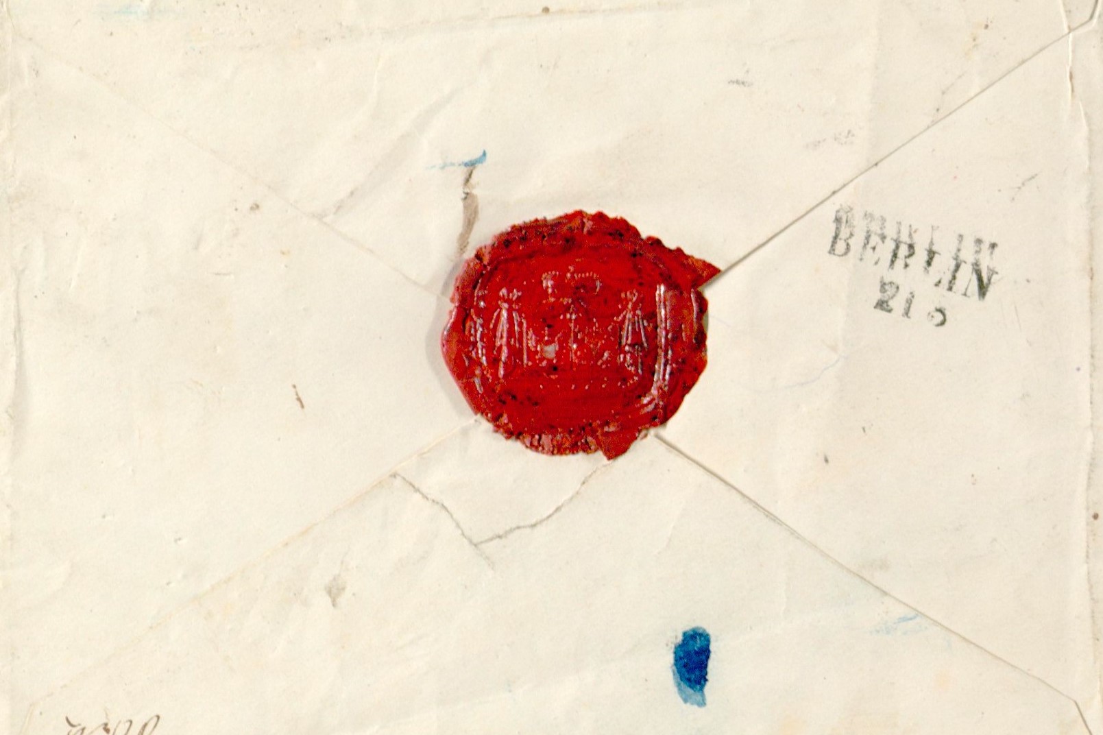 Fotografia przedstawia rewers białej koperty papierowej z czerwoną pieczęcią lakową. 